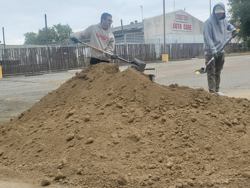 Two ABLED clients shoveling a large pile of dirt in ABLED's parking lot.