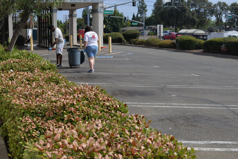 Two ABLED clients in the parking lot cleaning up trash, using PPE (gloves and grabbers) to safely pick up trash