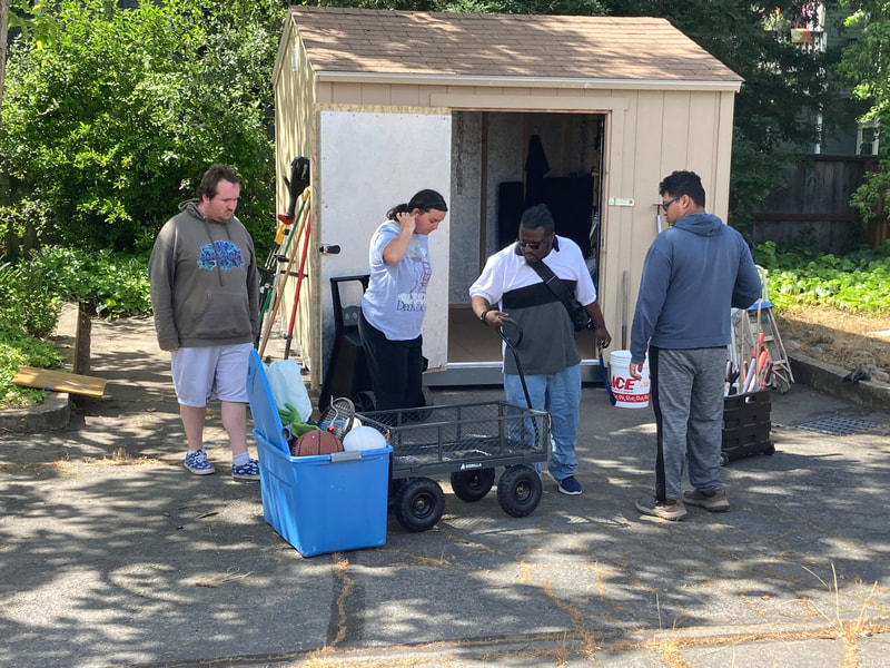ABLED clients standing in the parking lot at ABLED HQ, organizing the shed. There are gardening tools and recreational equipment in the picture